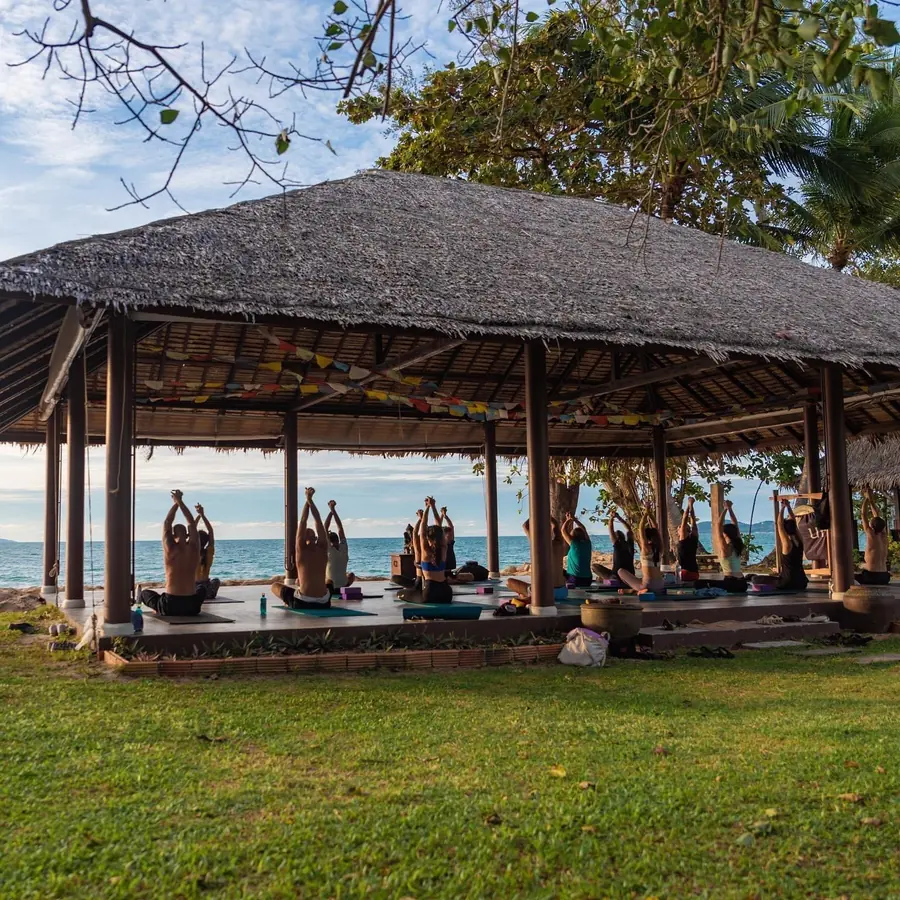 Yoga group practising in an open-air beachfront sala, sea on the horizon.
