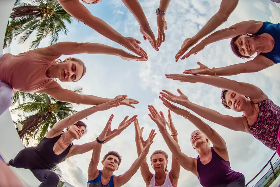 Fisheye view of a yoga group reaching their hands together overhead in a circle.