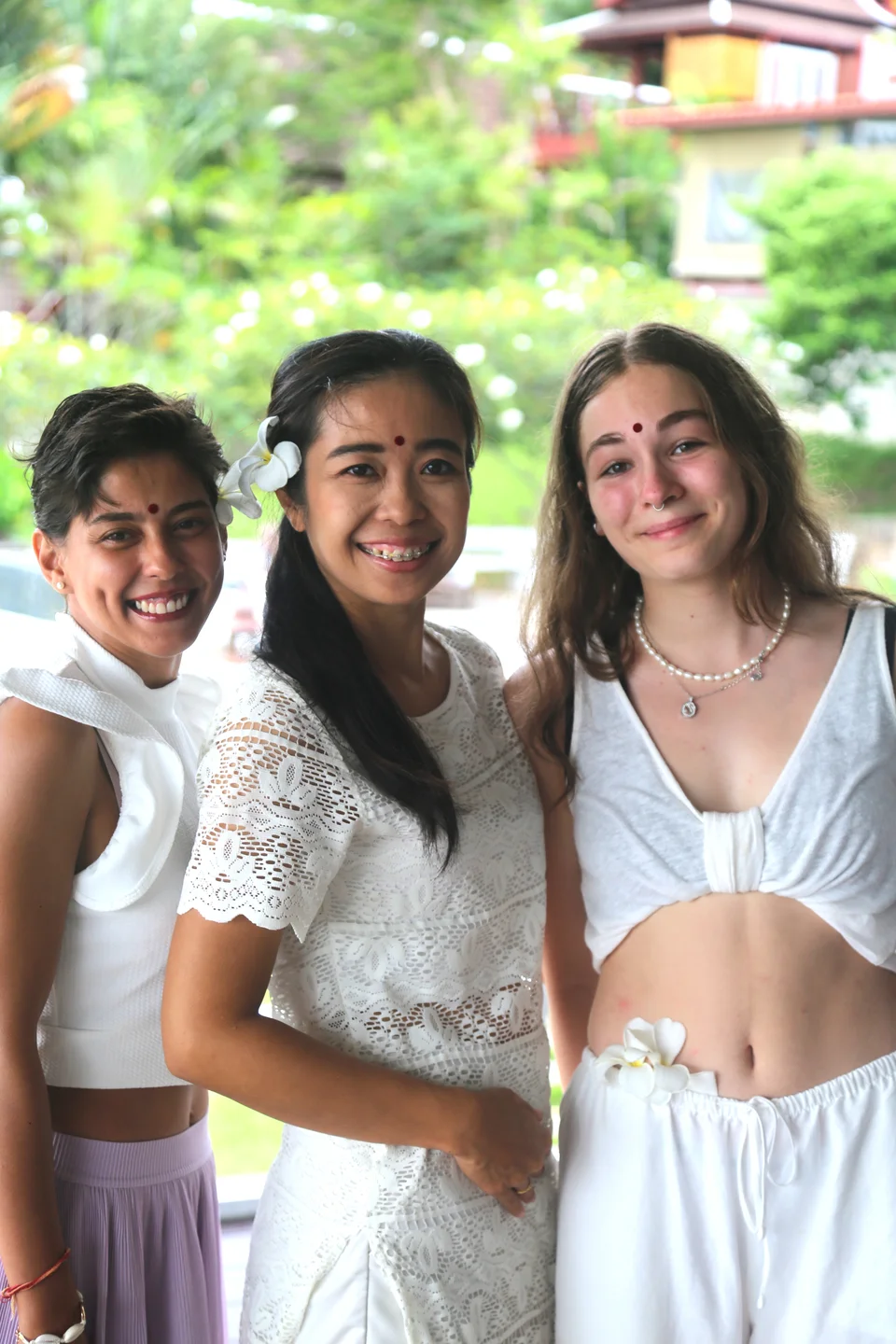 Three women smiling together outdoors with flowers in their hair.