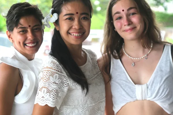 Three women smiling together outdoors with flowers in their hair.