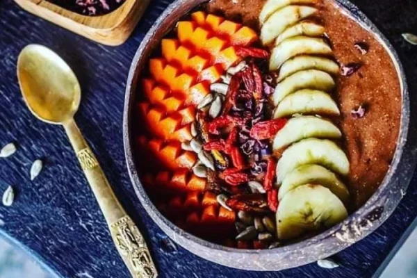 Smoothie bowl topped with sliced mango, banana, and seeds, with cacao on the side.