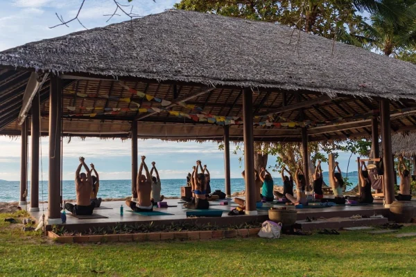 Yoga teacher training thailand students practicing in an open-air beachfront sala at dusk.
